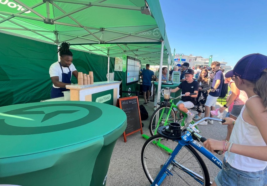 Animation Tour de France Vélo Smoothie, sous un stand, qui accueille un public nombreux dans le centre d’un village étape de la Grande Boucle.