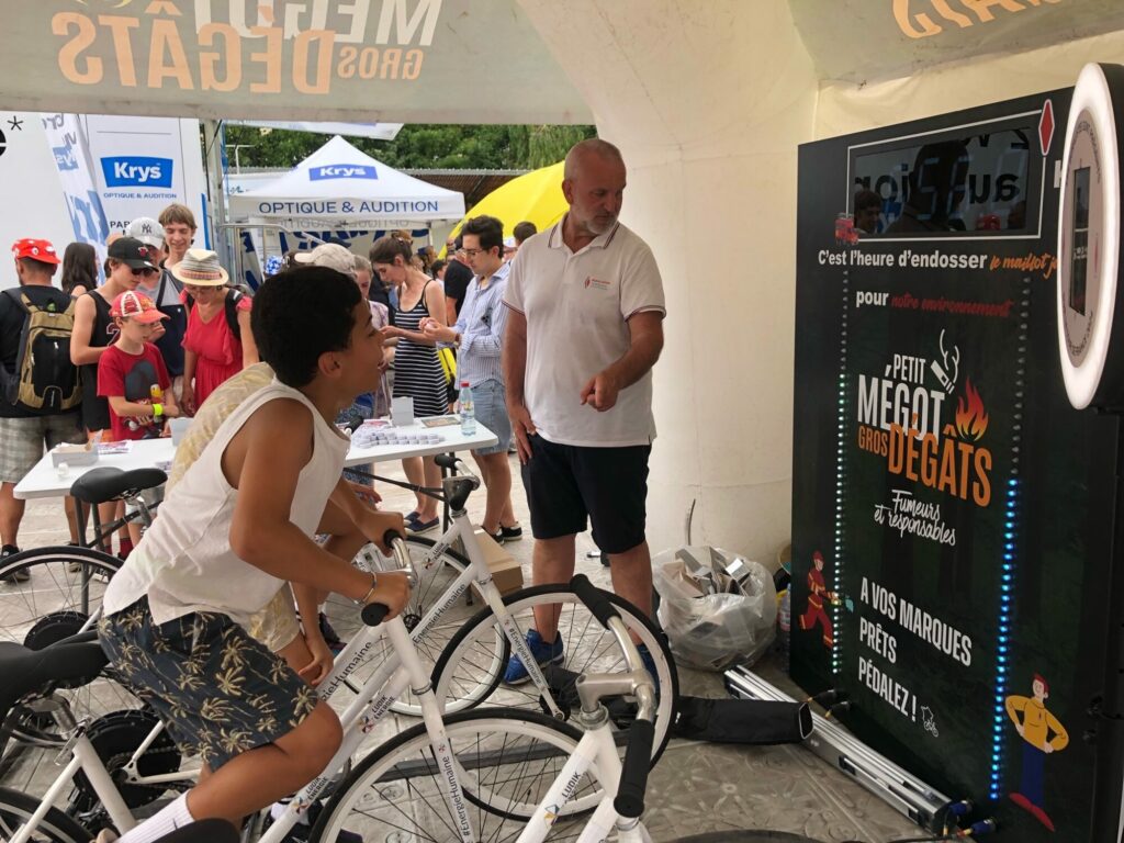  Deux enfants s’affrontant en duel sur l’animation Vélo Battle, avec un animateur, dans un stand du village du tour de France.