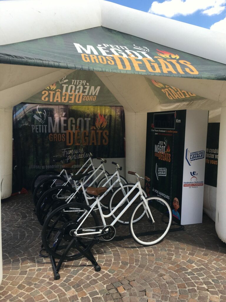 Animation Vélo Battle, constituée de quatre vélos reliés à un compteur de kilomètres, sous un stand du village du Tour de France.