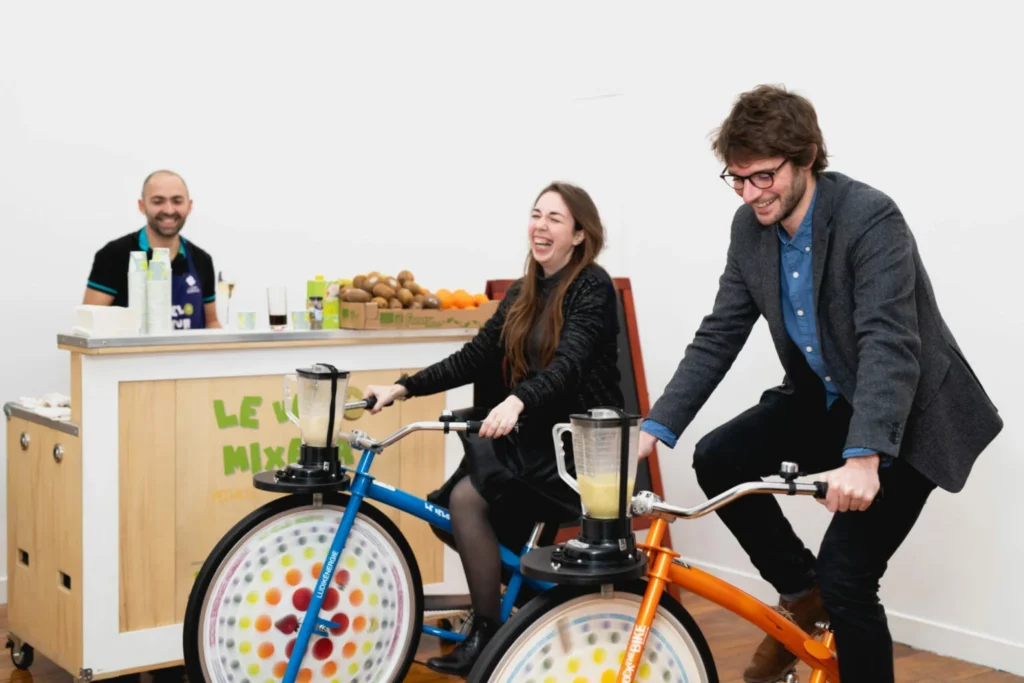Deux collaborateurs qui pédalent sur l’animation Vélo Mixeur et créent leur propre smoothie pour prendre une pause fruitée pendant un team building green.