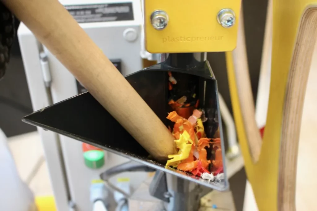 Plastique en miettes inséré dans une extrudeuse pour créer des objets en plastique recyclé lors d’une animation éco-responsable en entreprise.