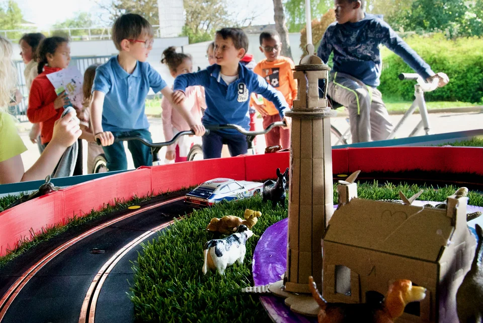 2 enfants font une course de slot car alimenté par des vélos générateurs d'électricité à l'occasion d'une fête de la mobilité