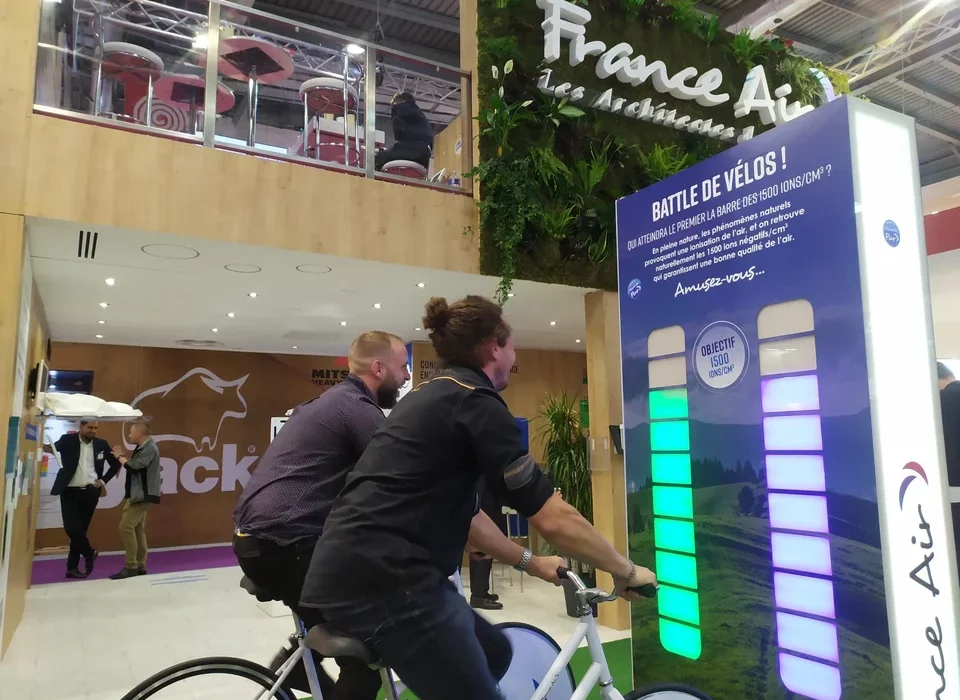 2 visiteurs remplissent une jauge d'énergie avec des vélos générateurs d'électricité sur un salon professionnel